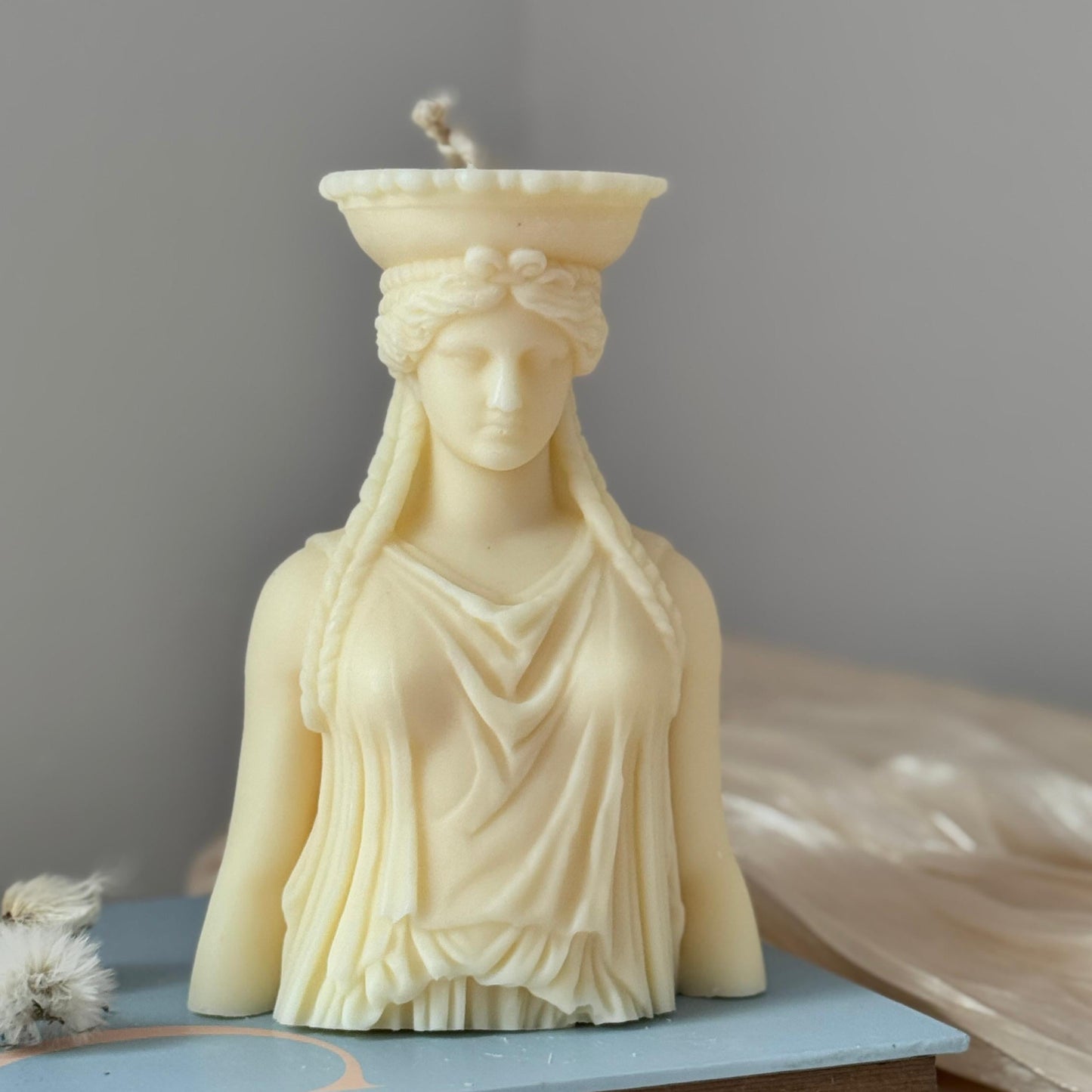 Candle shaped like a classical statue on a book with a plain background